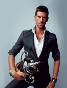 Novak Djokovic posing for a photo shot with a trophy in a grey suit and whit shirt