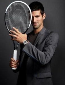 Novak Djokovic smiling in a suit and with a tennis racket