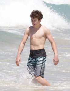 Nolan Gould shirtless on the beach going into a wave