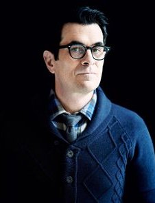 Ty Burrell with glasses in a blue shirt with a serious look